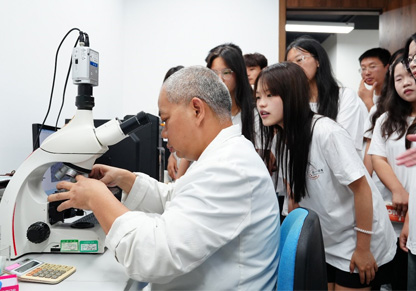 Man surrounded by university students looking into a microscope