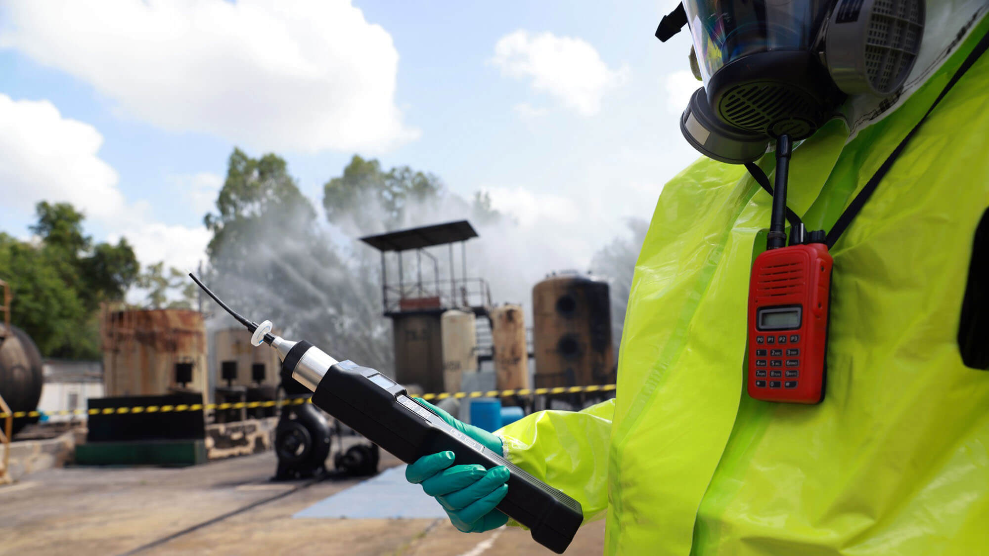 The male in a gas mask and hazmat suit holds the Toxic air detector in a chemically polluted environment and danger zone